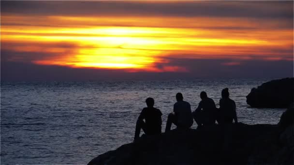 Groep van tieners zittend op een rots en genieten van de zonsondergang — Stockvideo