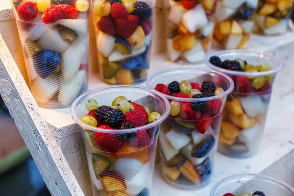Kubki plastikowe pokrojone owoce. Truskawka, blackberry, kiwi, ananas, maliny, śliwki, winogrona, melon na sprzedaż iść — Zdjęcie stockowe