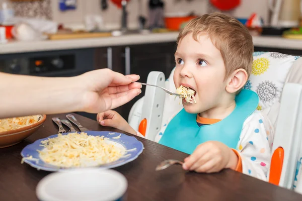 Mother feeding hungry boy in the highchair indoors — Stock Photo, Image