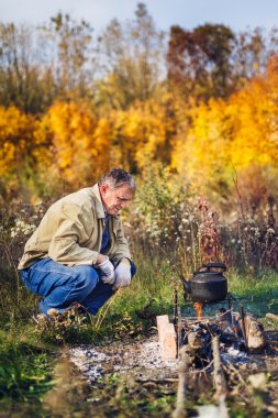 man boils sooty kettle on the fire