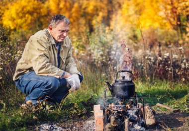man boils sooty kettle on the fire