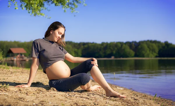pregnant woman sitting on beach near lake