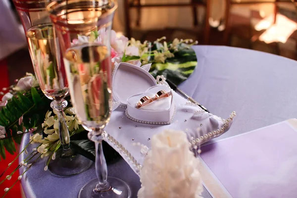 Anillos de boda y dos copas de vino blanco sobre fondo de tela de satén — Foto de Stock