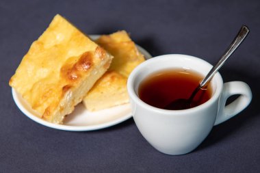 Beyaz bardakta çay, çay tabağında da kremalı güveç. Kahvaltıda. Yakın plan. Seçici odak.