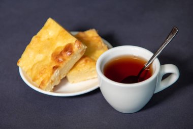 Beyaz bardakta çay, çay tabağında da kremalı güveç. Kahvaltıda. Yakın plan. Seçici odak.