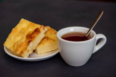 Beyaz bardakta çay, çay tabağında da kremalı güveç. Kahvaltıda. Yakın plan. Seçici odak.