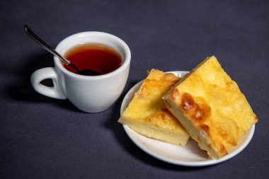 Beyaz bardakta çay, çay tabağında da kremalı güveç. Kahvaltıda. Yakın plan. Seçici odak.