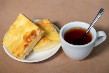 Beyaz bardakta çay, çay tabağında da kremalı güveç. Kahvaltıda. Yakın plan. Seçici odak.