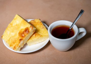 Beyaz bardakta çay, çay tabağında da kremalı güveç. Kahvaltıda. Yakın plan. Seçici odak.