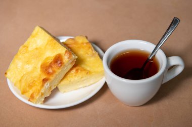 Beyaz bardakta çay, çay tabağında da kremalı güveç. Kahvaltıda. Yakın plan. Seçici odak.