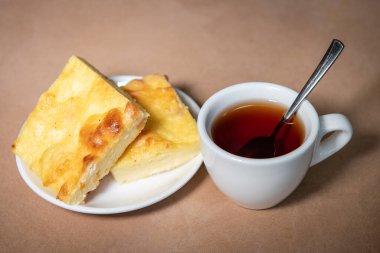 Beyaz bardakta çay, çay tabağında da kremalı güveç. Kahvaltıda. Yakın plan. Seçici odak.