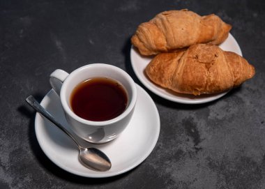 Bir fincan çay ya da kahve, içinde kruvasan olan beyaz bir fincan. Kahvaltıda. Yakın plan. Seçici odak.