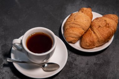 Bir fincan çay ya da kahve, içinde kruvasan olan beyaz bir fincan. Kahvaltıda. Yakın plan. Seçici odak.