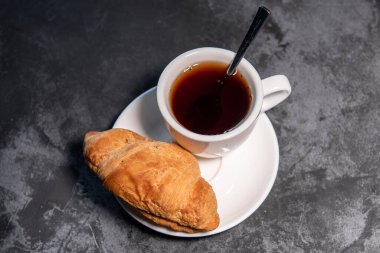 Bir fincan çay ya da kahve, içinde kruvasan olan beyaz bir fincan. Kahvaltıda. Yakın plan. Seçici odak.