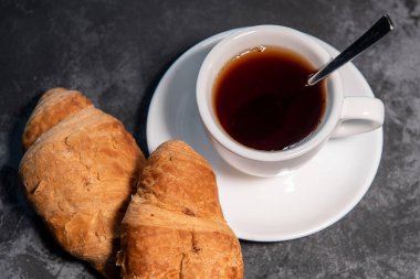 Bir fincan çay ya da kahve, içinde kruvasan olan beyaz bir fincan. Kahvaltıda. Yakın plan. Seçici odak.