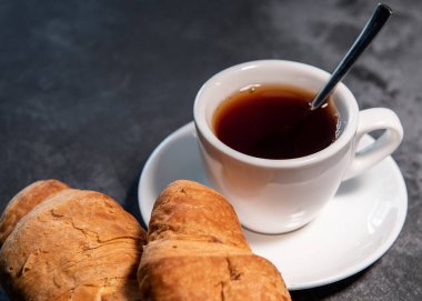 Bir fincan çay ya da kahve, içinde kruvasan olan beyaz bir fincan. Kahvaltıda. Yakın plan. Seçici odak.