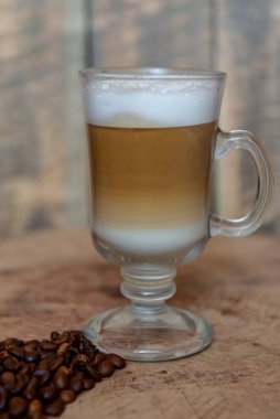 Cam bardakta Latte. Kapuçino. Köpüklü kahve. Ahşap arka. Yakın plan. Kahve çekirdeği. Sabah kahvesi
