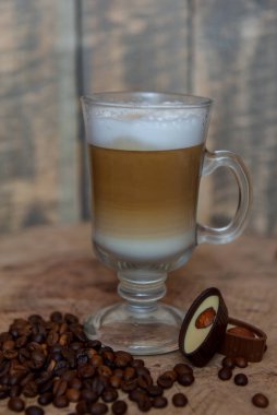 Şeffaf bardakta kahve ve tahta arka planda bir kalem. Kapuçino. Kahve çekirdeği. Fındıklı çikolatalı şekerler. Sabah kahve konsepti.