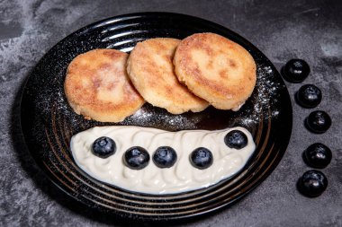 Siyah tabakta ekşi krema ve yaban mersinli cheesecake (gözleme). Sağlıklı ve lezzetli bir kahvaltı. Yakın plan.