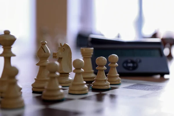 Chess clock and white chess pieces on the board