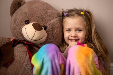 Seçici odaklanma. At kuyruklu şirin küçük kız oyuncak ayıya sarılıyor, gülümsüyor ve kameraya bakıyor. Ev eğlencesi konsepti. Yakın plan.