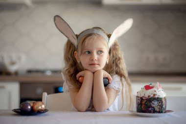 Tavşan kulaklı şirin bir kız elinde iki renkli puantiyeli yumurta tutuyor. Sürpriz Paskalya pastası ve çocuk portresi. Paskalya kutlaması, bahar tatili konsepti. Çocukların eğlencesi.