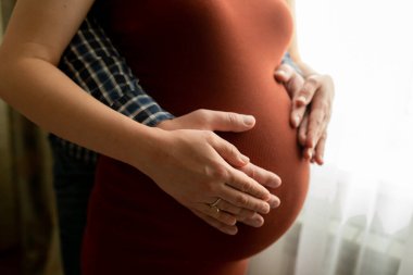 Ebeveynlerin elleri evdeki hamile kadının karnına dokunuyor. Hamileliğin üçüncü üç ayı, kocaya yardım ve destek, eş doğum, kasılmalar, yetiştirme. Seçici odak