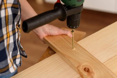 Tahta bir bankta, bir tahta parçasına vida delme matkabını kapat. Ahşap bankta çalışan bir kadın. DIY meraklısı.