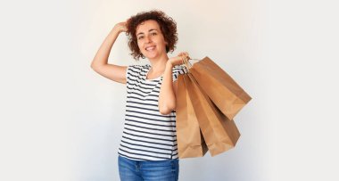 Stüdyo arka planında alışveriş torbaları olan beyaz saçlı, çizgili tişört ve kot pantolon giyen genç bir kadın.