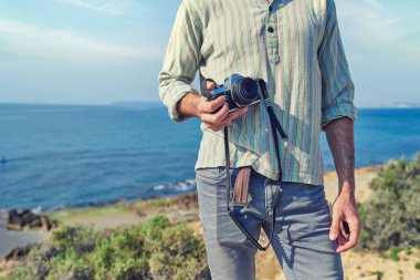 Genç turist kamerasını turist plajında tutuyor.