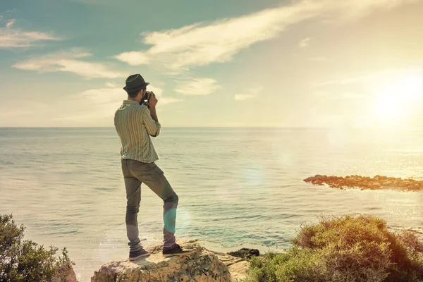 Genç gezgin, günbatımını gösteren eski fotoğraf makinesiyle bir tepeden ya da deniz üzerinde gün batımını seyrederken fotoğraf çeker.
