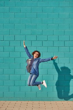 Güneşli bir günde parlak mavi bir duvara atlayan mutlu bir kadının ön görüntüsü. Yüksek kalite fotoğraf.