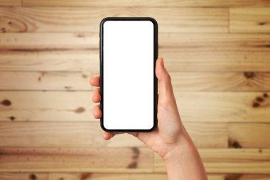 A woman's hand holds a mobile phone with the blank screen on a wooden background