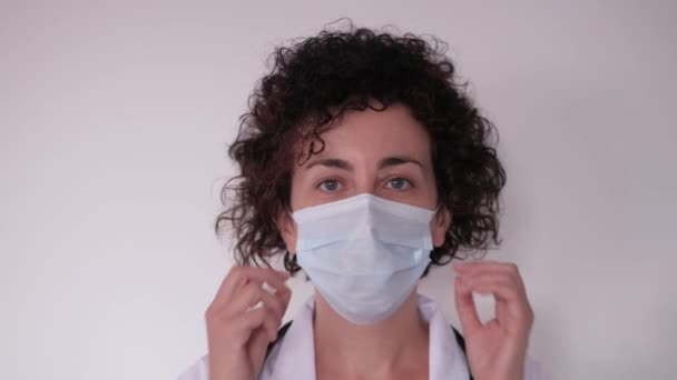 En kvinnlig läkare tar bort sin ansiktsmask medan hon tittar på kameran — Stockvideo
