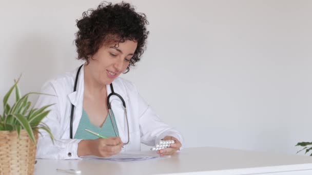 Lékařka připravuje předpis na prášky, které sedí v její kanceláři. — Stock video