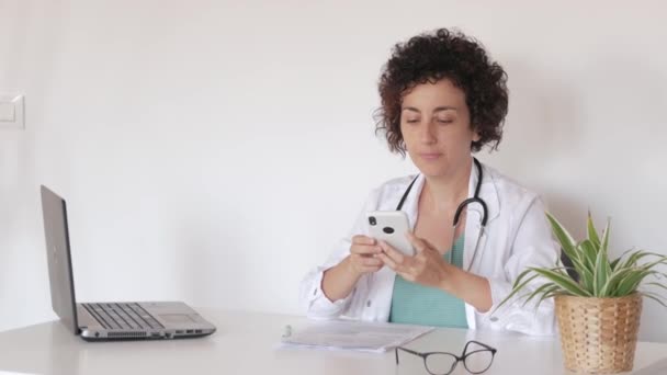 En kvindelig læge tager sig af en patient via telefon på hendes kontor – Stock-video