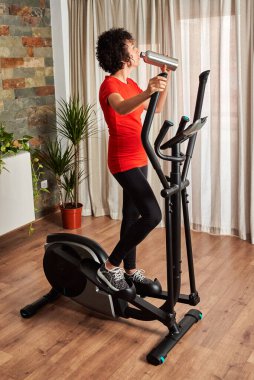 Çapraz eğitim eliptik ile evde eğitim görürken su içen kadın