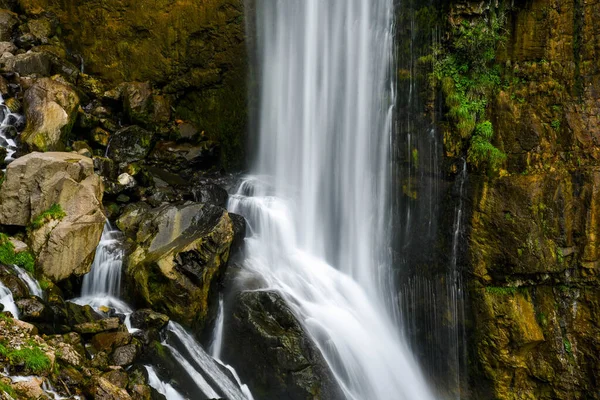 Beautiful long exposure photo of a waterfall in switzerland rushing down a cliff and bursting onto a steep rocky mountainside.