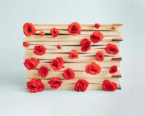 Flowers and paths of red roses arranged between the leaves of books placed on a light blue background. Minimal concept