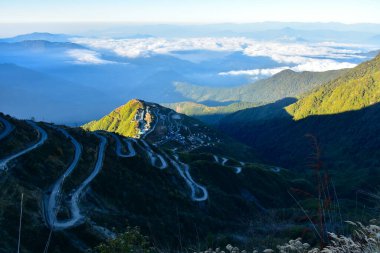 Dağ zirvesi sabahın erken saatlerinde altın güneş ışığıyla yıkandı, yamaçta yılan otobanı var.