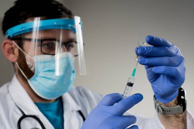 Beyaz önlüklü yakışıklı beyaz erkek doktor enfeksiyoncusunun yakın plan portresi. Klinikteki dolapta oturmuş hasta doktor konseptiyle internet kamerasından görüntülü konuşma yapıyor.