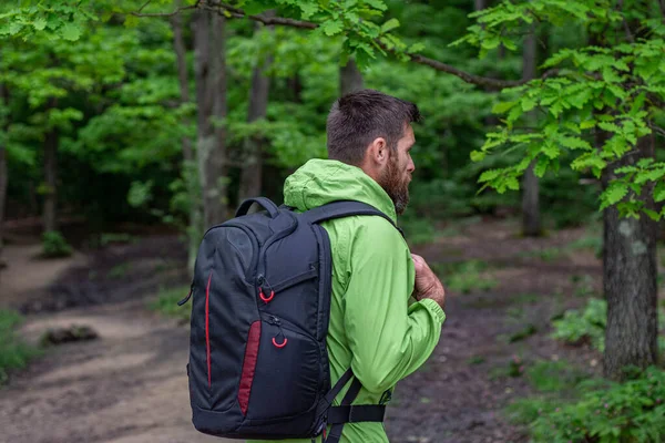 Photo of man with backpack in forest . Adventurer with a hood(view from back) walking through
