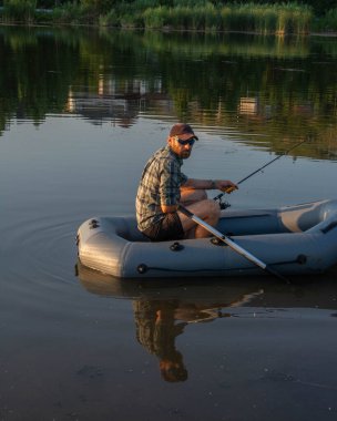 Şişme tekneyle gölde balık tutan olgun bir adam.