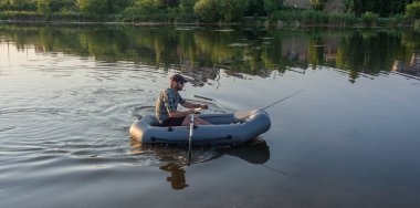 Şişme tekneyle gölde balık tutan olgun bir adam.
