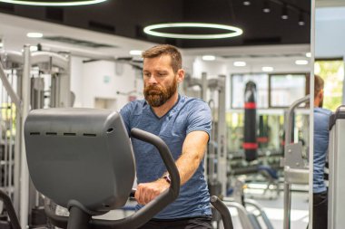 Sabit egzersiz bisikleti süren, spor salonunda sakal eğitimi almış aktif bir adam. Spor ve karantina.