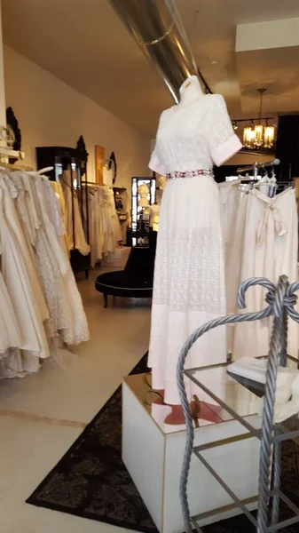 inside a vintage store focusing on bridal gowns with mannequin of bridal gown in foreground with various gowns and decor in the background