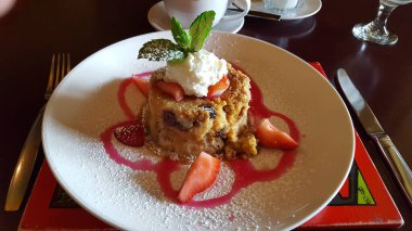 Çilek tatlısı, pudra şekeri ve beyaz bir tabakta ekmek pudingi. Gündüz vakti çilekli çiselemeli, yatay çekim.