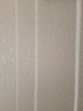 Pencere perdeleri ve içerideki dikey çekimler tarafından oluşturulan desenli beyaz bir duvardaki gölgeler.