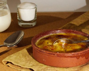 Bir fincan şeker ve bir fincan sütle süslenmiş peçeteye katalan kremasına batırılmış kaşık. Ahşap masada.