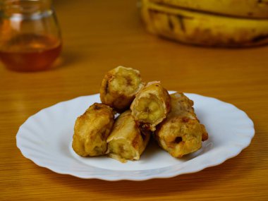 Muz ve balla süslenmiş beyaz bir tabakta olgun muz dilimleri.